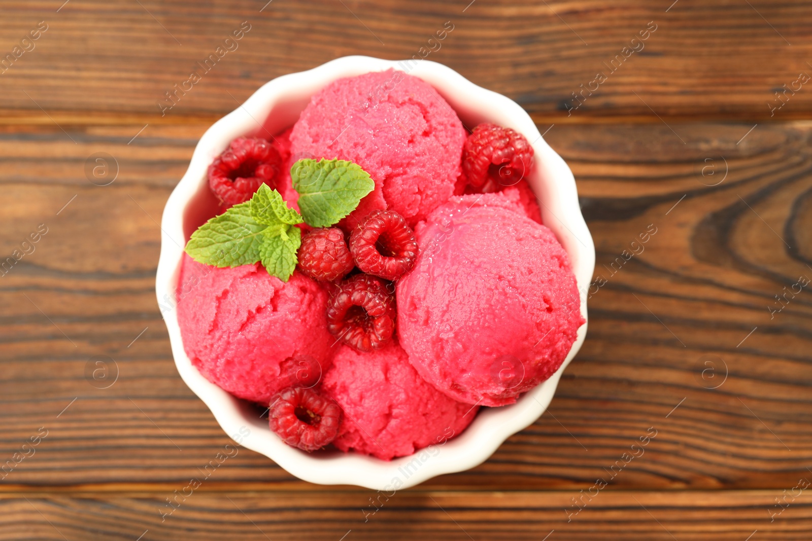 Photo of Delicious raspberry sorbet, fresh berries and mint in bowl on wooden table, top view