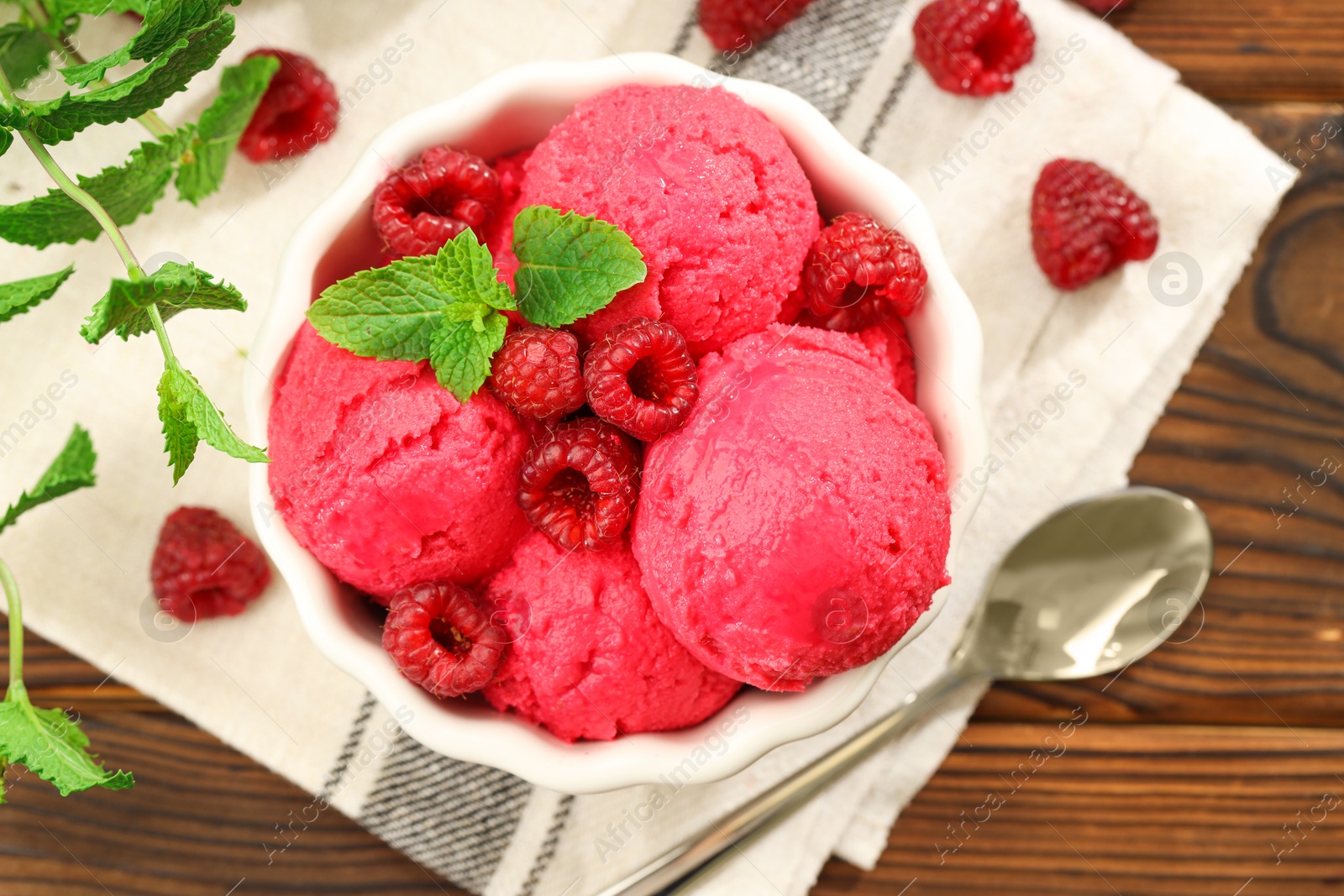 Photo of Delicious raspberry sorbet in bowl, fresh berries, mint and spoon on wooden table, flat lay