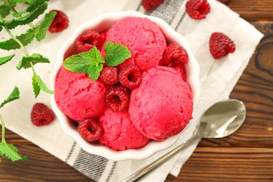 Photo of Delicious raspberry sorbet in bowl, fresh berries, mint and spoon on wooden table, flat lay