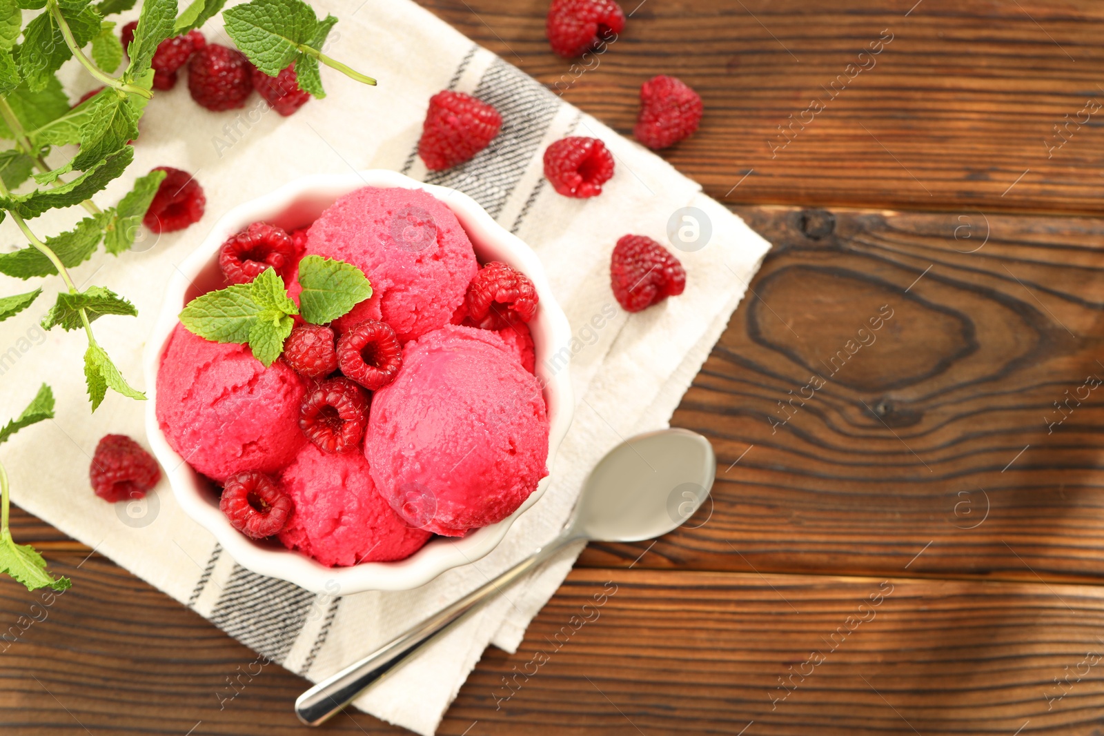 Photo of Delicious raspberry sorbet in bowl, fresh berries, mint and spoon on wooden table, flat lay. Space for text