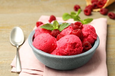 Photo of Delicious raspberry sorbet with fresh berries in bowl and spoon on wooden table, closeup