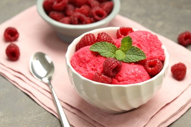 Photo of Delicious raspberry sorbet with fresh berries in bowl and spoon on gray textured table, closeup