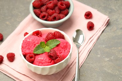 Delicious raspberry sorbet with fresh berries in bowl and spoon on gray textured table