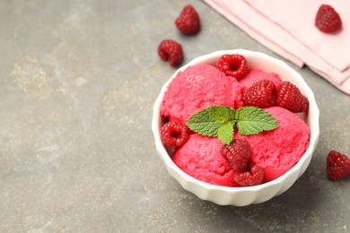 Photo of Delicious raspberry sorbet, fresh berries and mint in bowl on gray textured table, space for text