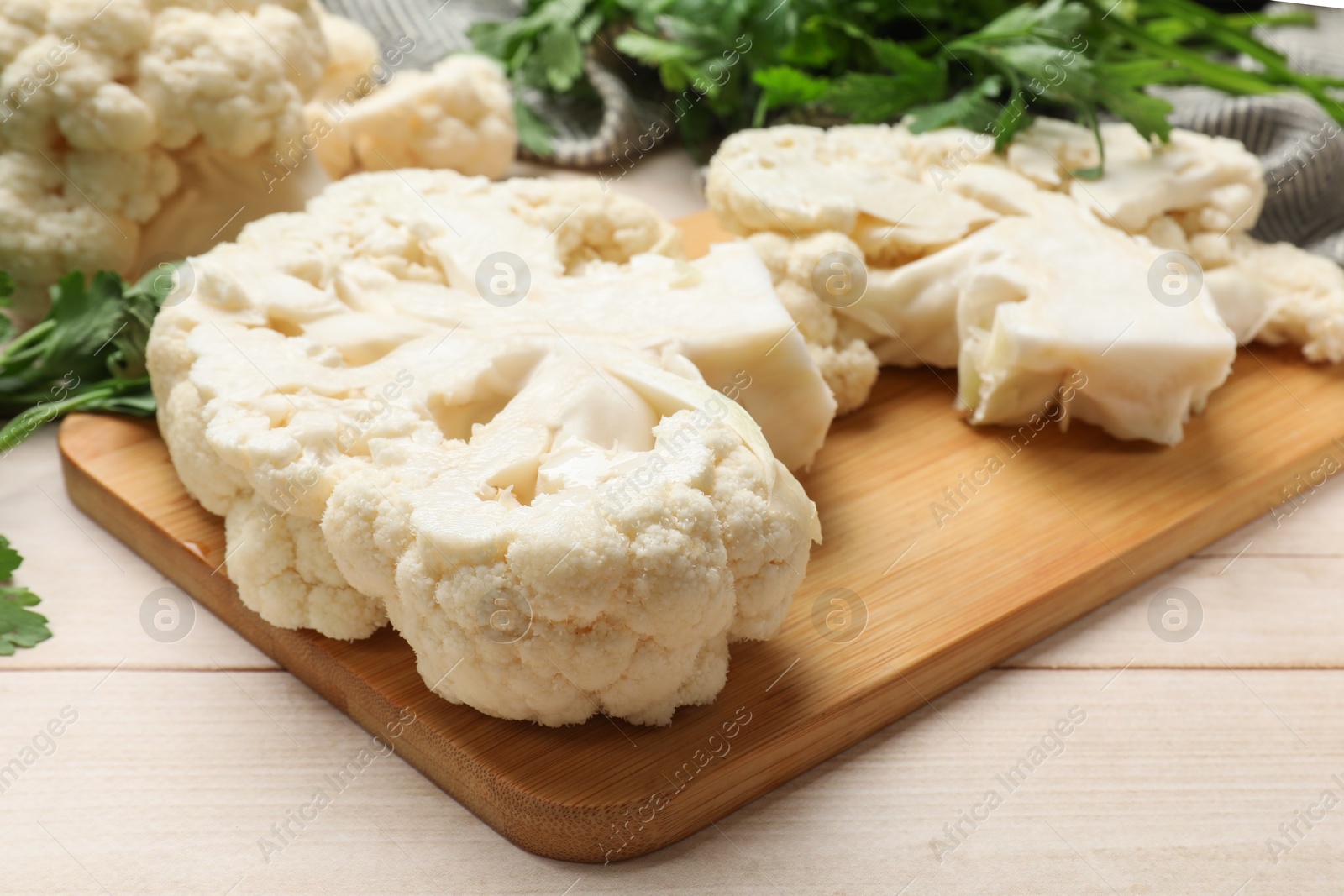 Photo of Uncooked cauliflower steaks and parsley on wooden table, closeup