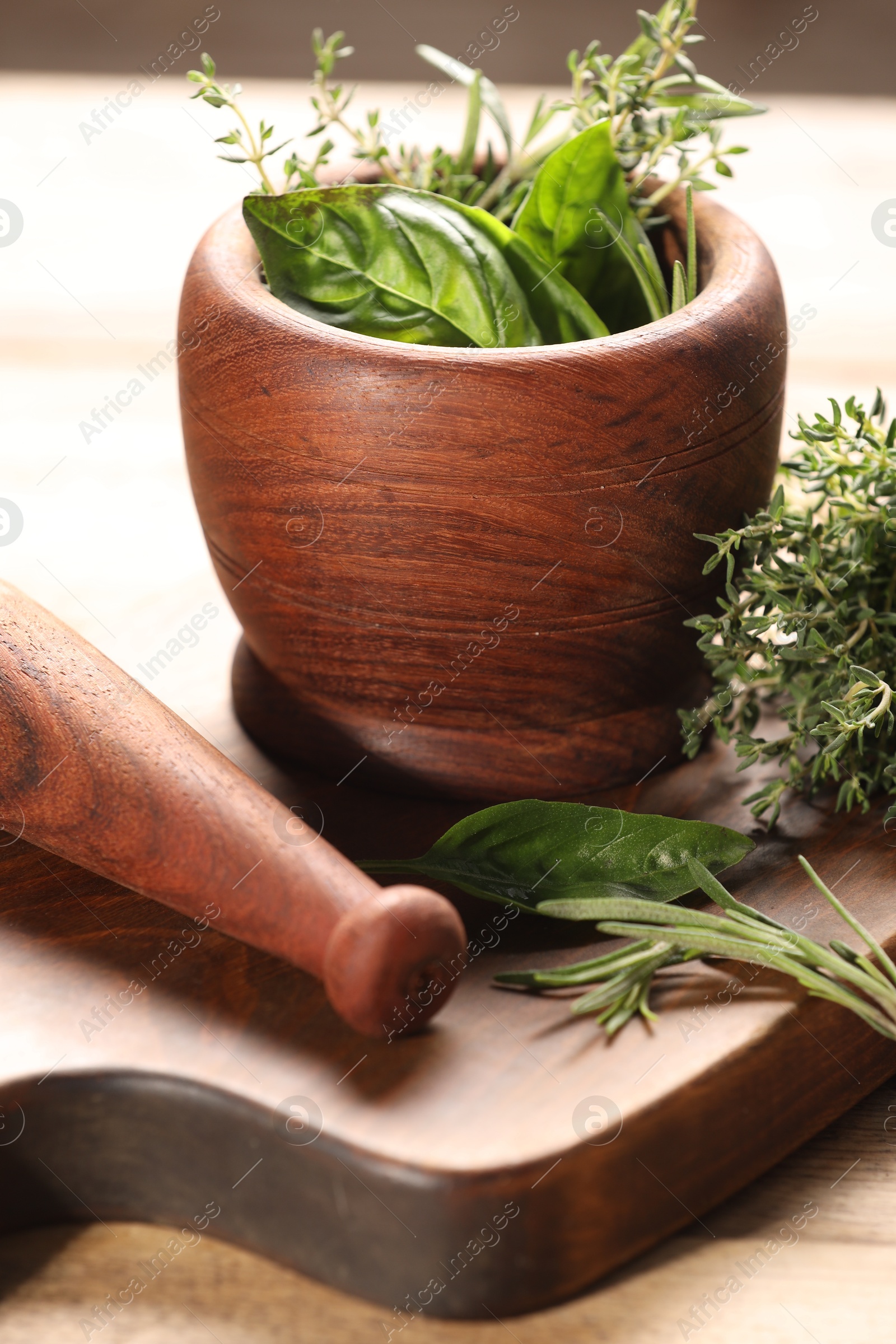 Photo of Different fresh herbs in mortar with pestle on wooden table