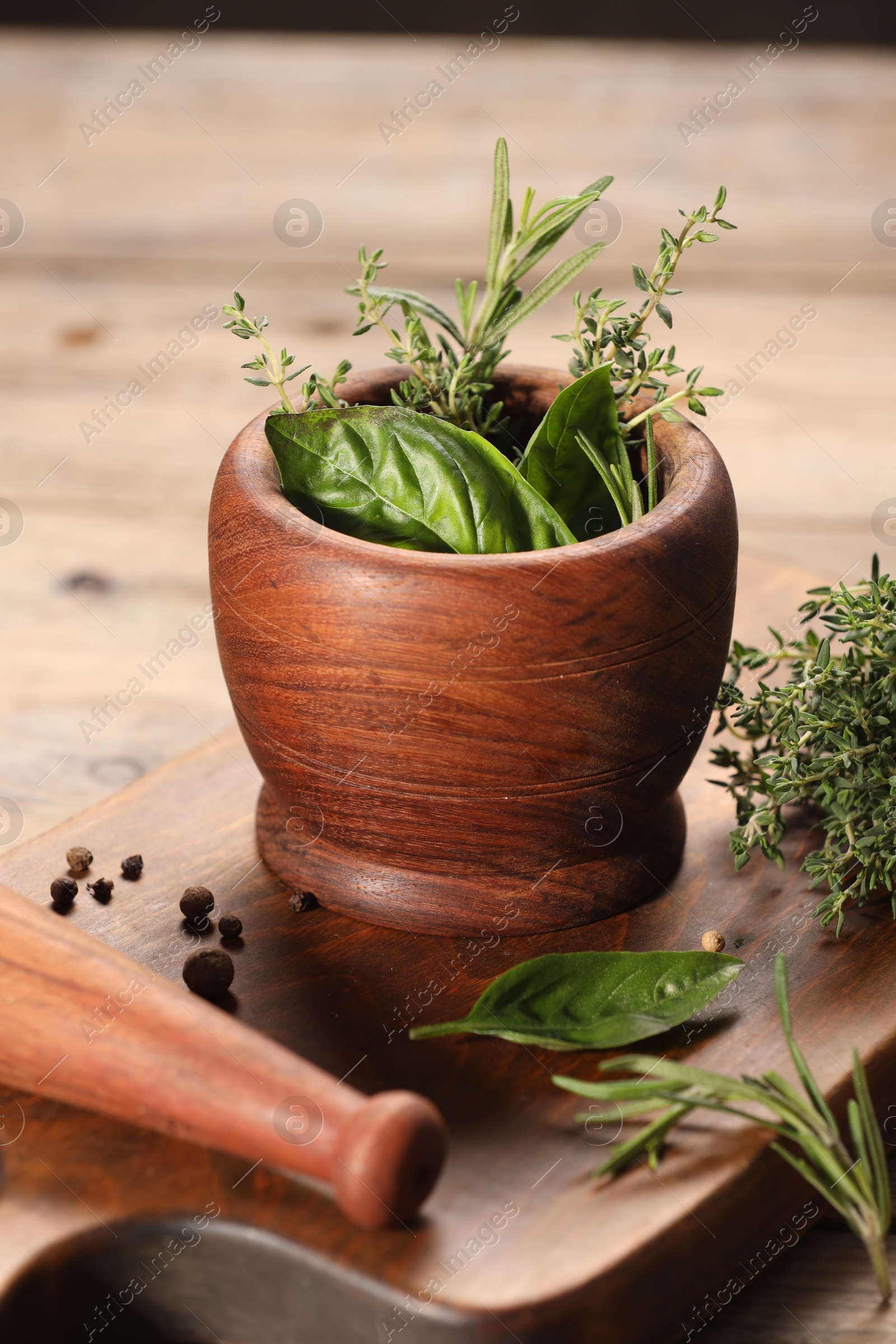 Photo of Different fresh herbs in mortar with pestle on wooden table