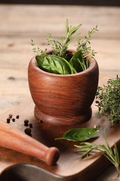 Photo of Different fresh herbs in mortar with pestle on wooden table