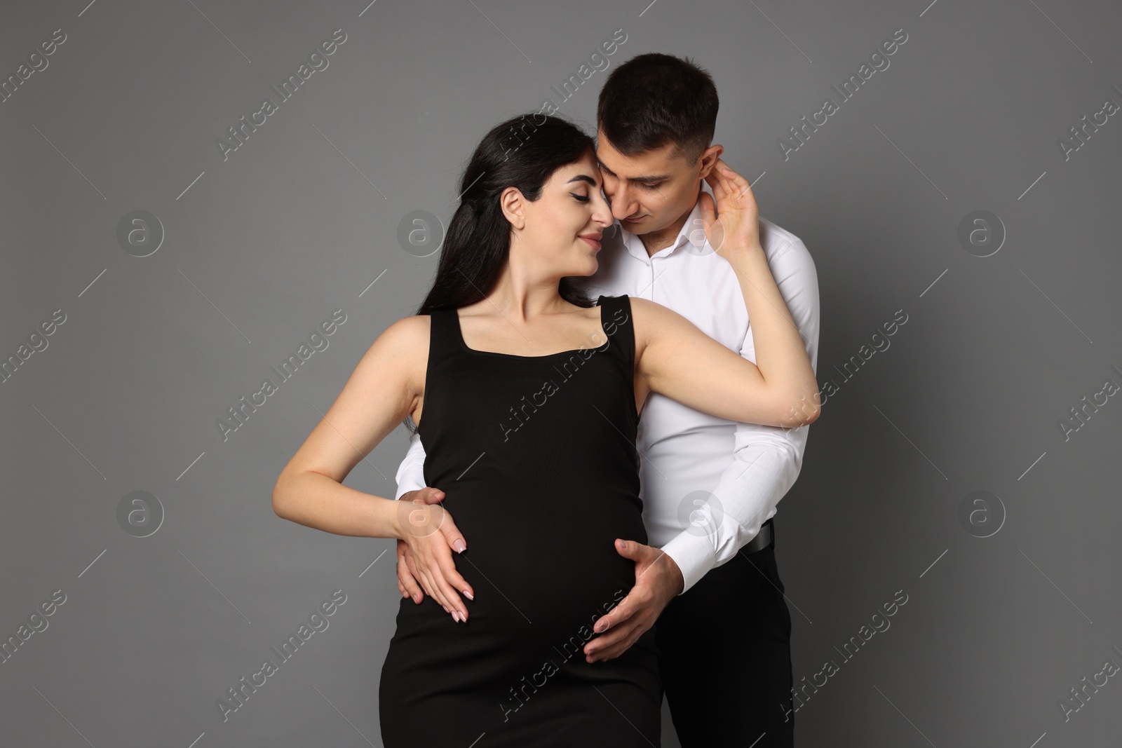 Photo of Beautiful pregnant woman with her husband on grey background