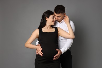 Beautiful pregnant woman with her husband on grey background