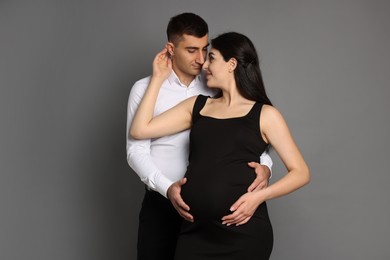 Beautiful pregnant woman with her husband on grey background