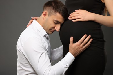 Photo of Man touching his pregnant wife's belly on grey background