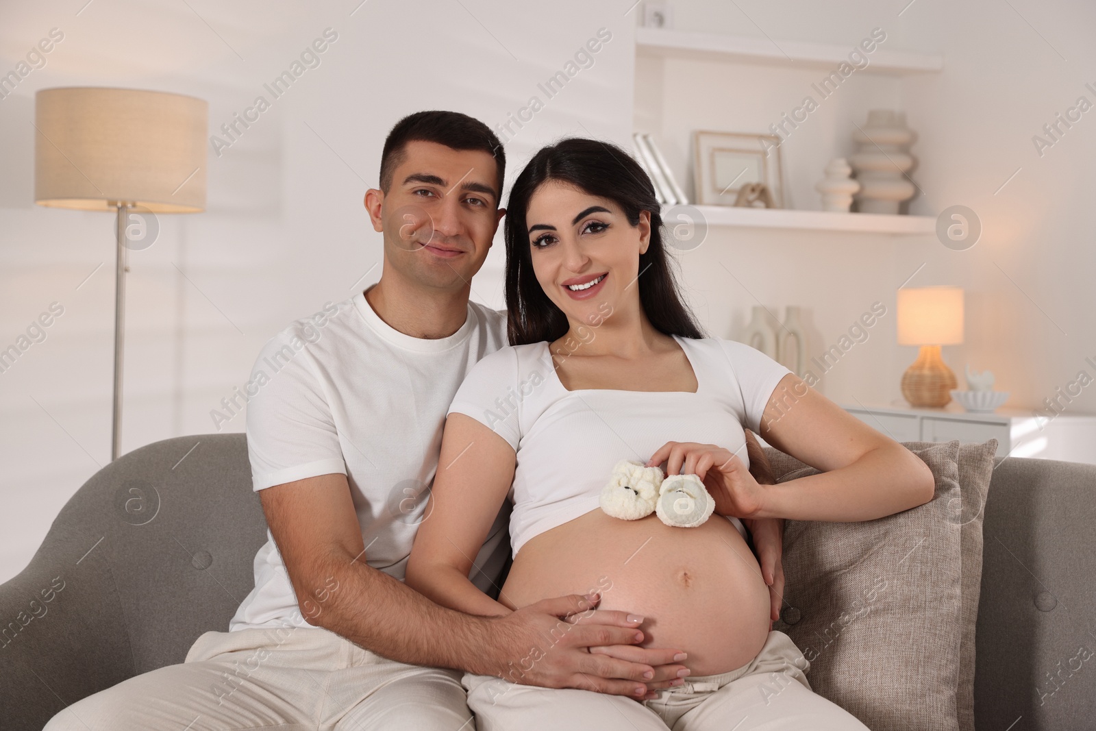 Photo of Portrait of beautiful pregnant woman with baby booties and her husband at home