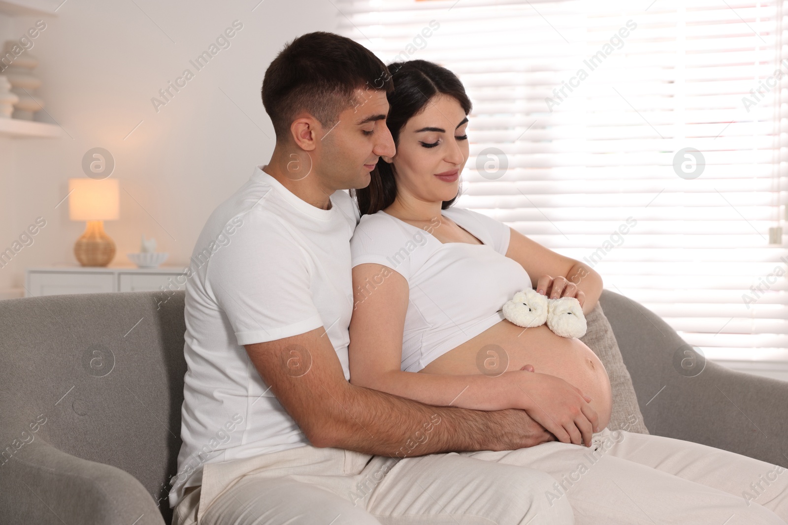 Photo of Beautiful pregnant woman with baby booties and her husband at home