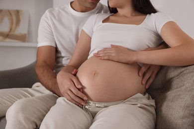 Man touching his pregnant wife's belly indoors, closeup