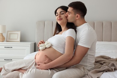 Photo of Beautiful pregnant woman with baby booties and her husband in bedroom