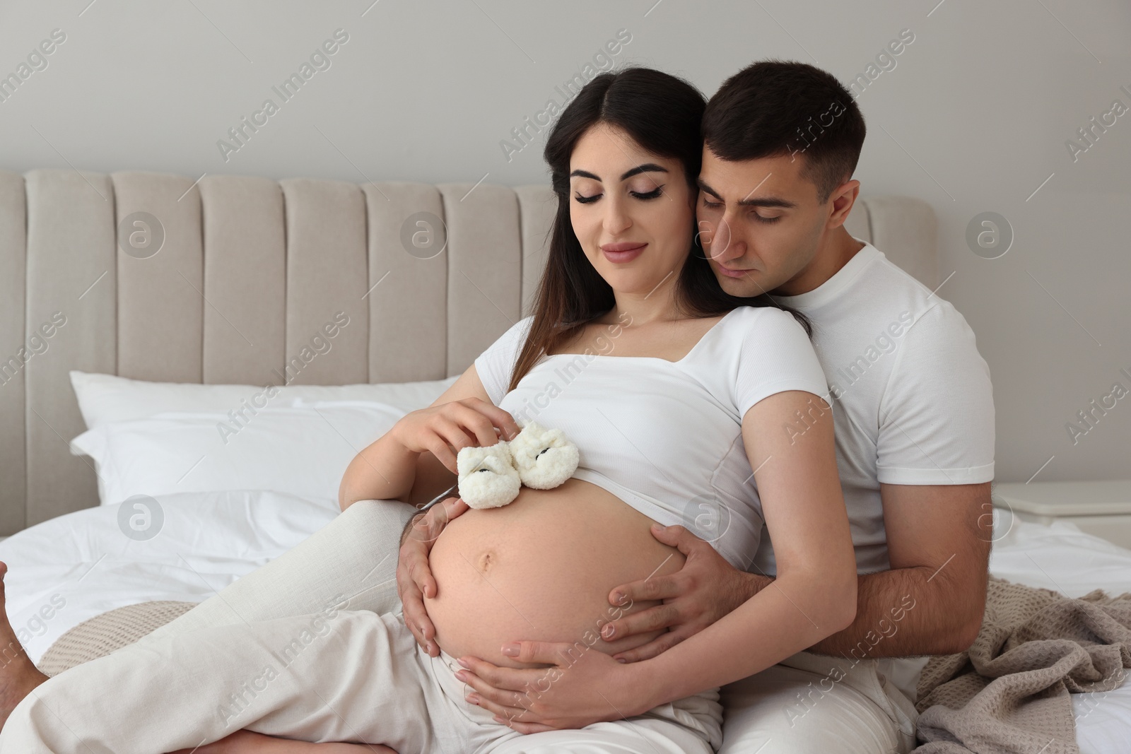 Photo of Beautiful pregnant woman with baby booties and her husband in bedroom