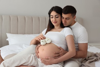 Photo of Beautiful pregnant woman with baby booties and her husband in bedroom