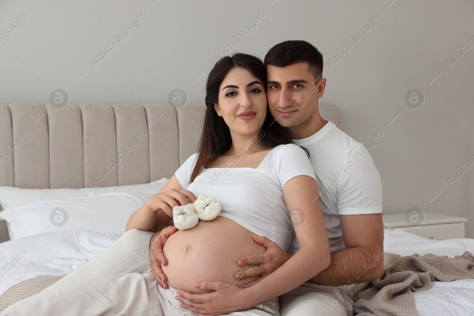 Photo of Beautiful pregnant woman with baby booties and her husband in bedroom