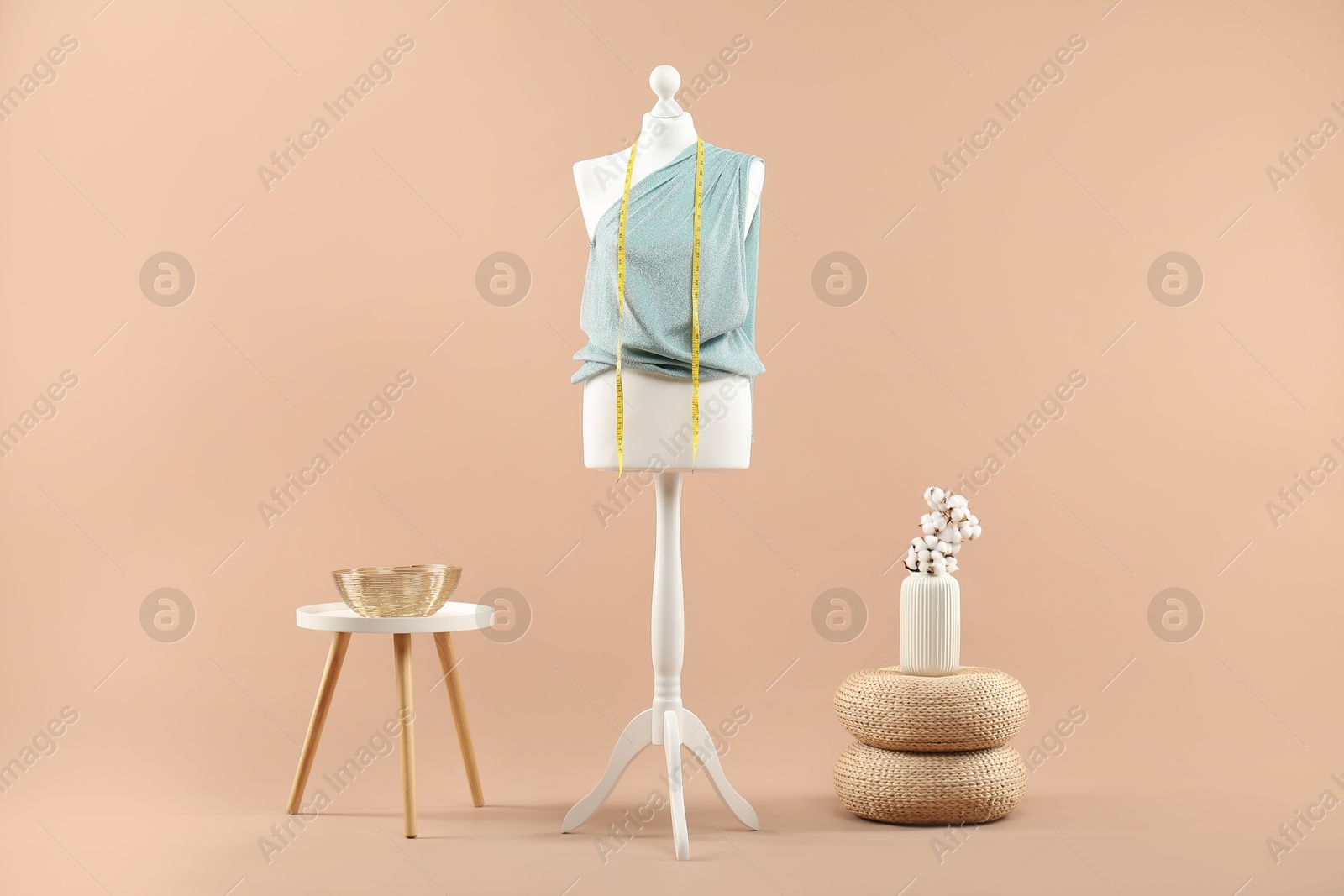 Photo of Mannequin with cloth, measuring tape, vase and stool on beige background