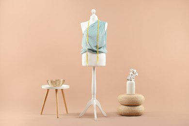 Mannequin with cloth, measuring tape, vase and stool on beige background