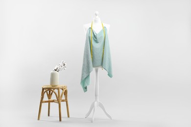 Photo of Mannequin, cloth, measuring tape and stool on light grey background