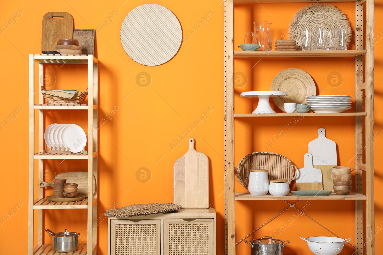 Photo of Wooden storage stands and cabinet with kitchenware near orange wall indoors