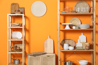 Photo of Wooden storage stands and cabinet with kitchenware near orange wall indoors