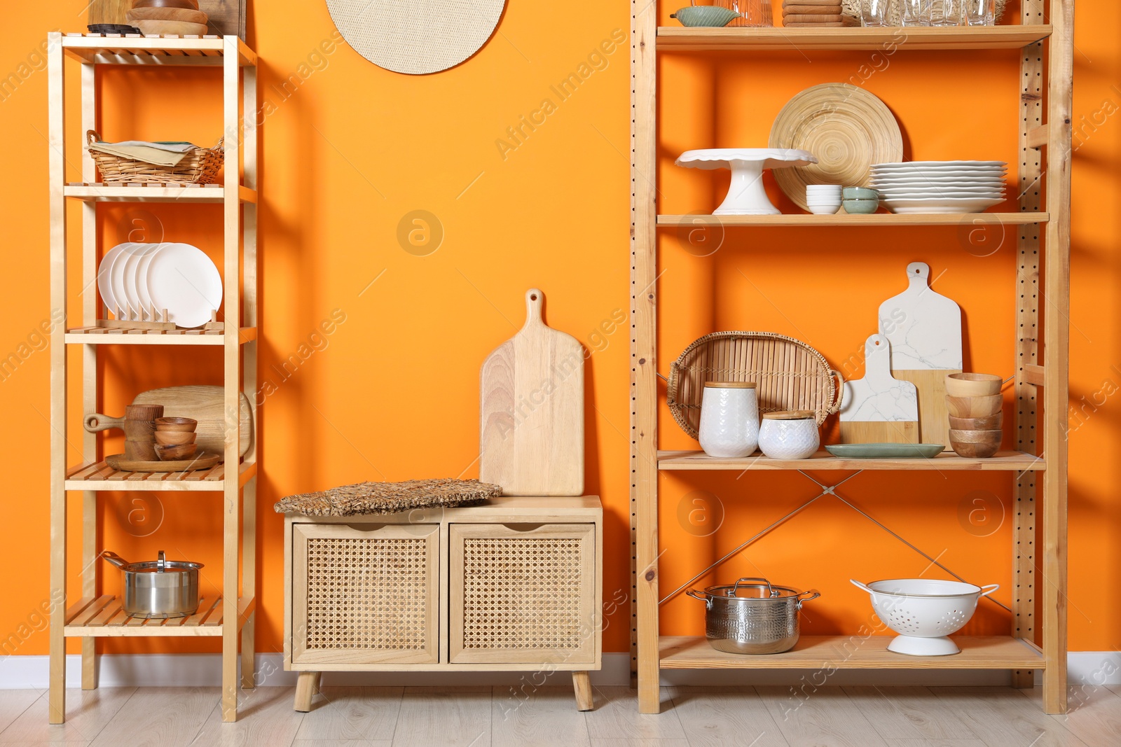 Photo of Wooden storage stands and cabinet with kitchenware near orange wall indoors