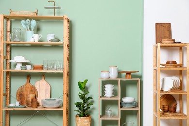 Wooden storage stands and shelving unit with kitchenware near green wall indoors