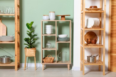 Photo of Wooden storage stands and shelving unit with kitchenware near green wall indoors