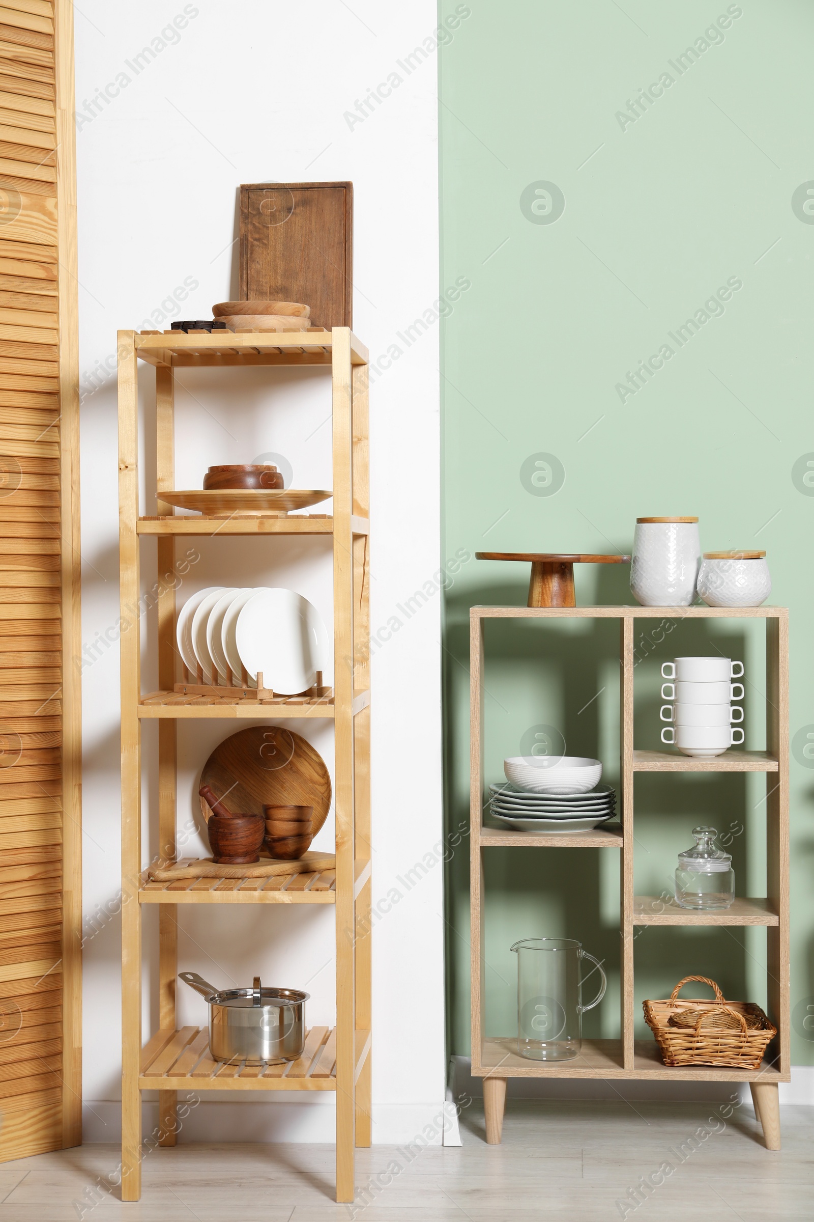 Photo of Wooden storage stand and shelving unit with kitchenware near green wall indoors