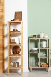 Wooden storage stand and shelving unit with kitchenware near green wall indoors