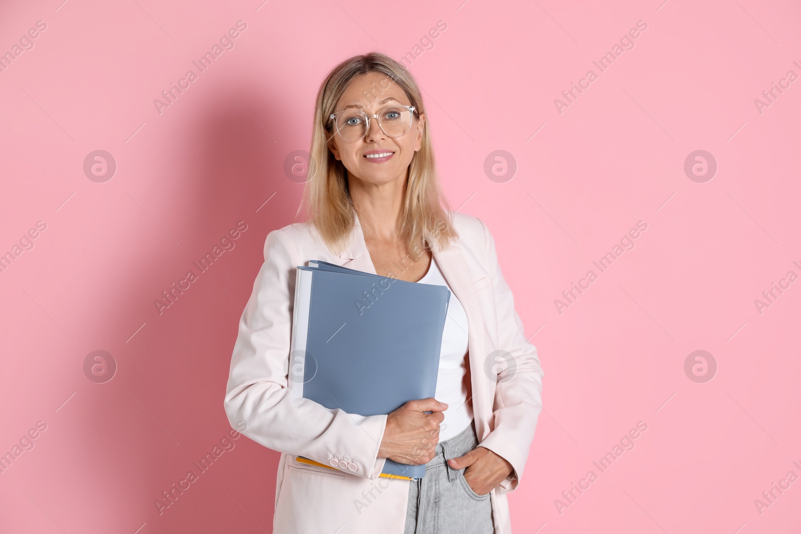 Photo of Portrait of beautiful smiling woman in glasses with folders on pink background