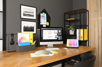 Designer's workplace with computer, tablet, stationery and palettes on wooden table indoors