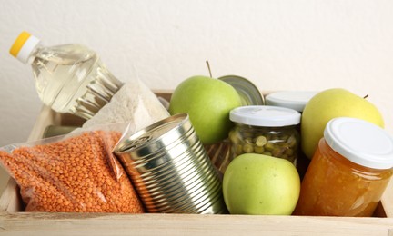 Photo of Different donation food products in crate on light background, closeup