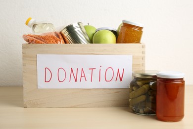 Photo of Different donation food products in crate on wooden table