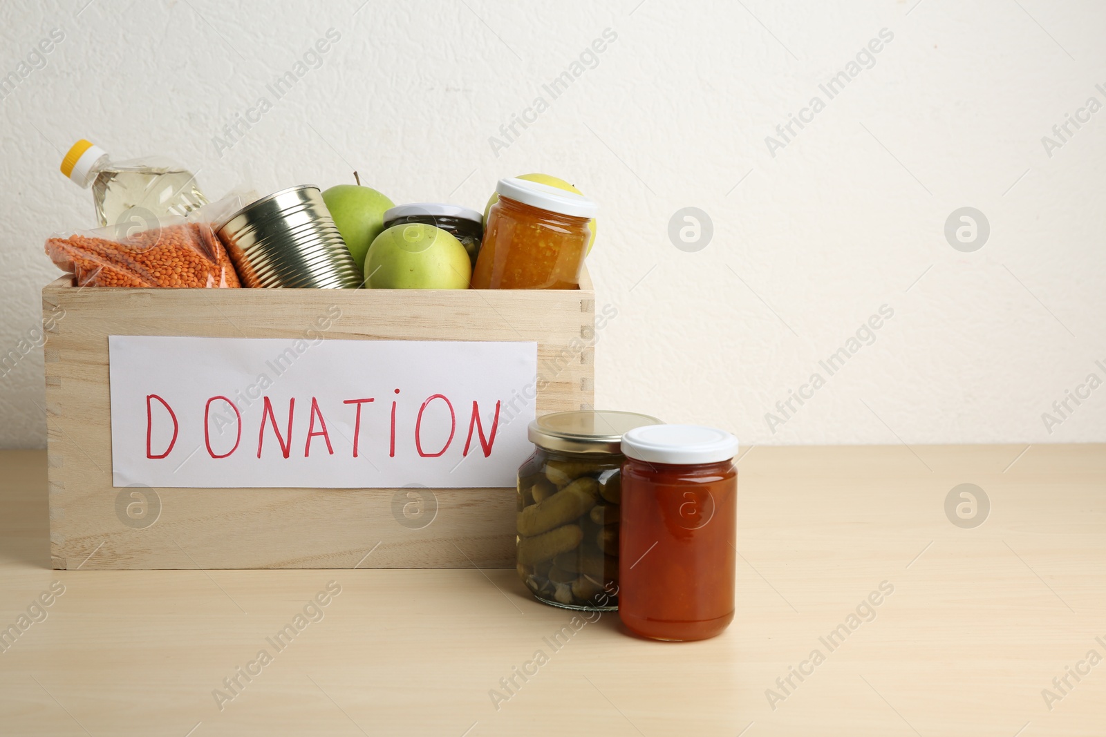 Photo of Different donation food products in crate on wooden table. Space for text