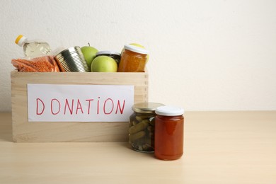 Photo of Different donation food products in crate on wooden table. Space for text