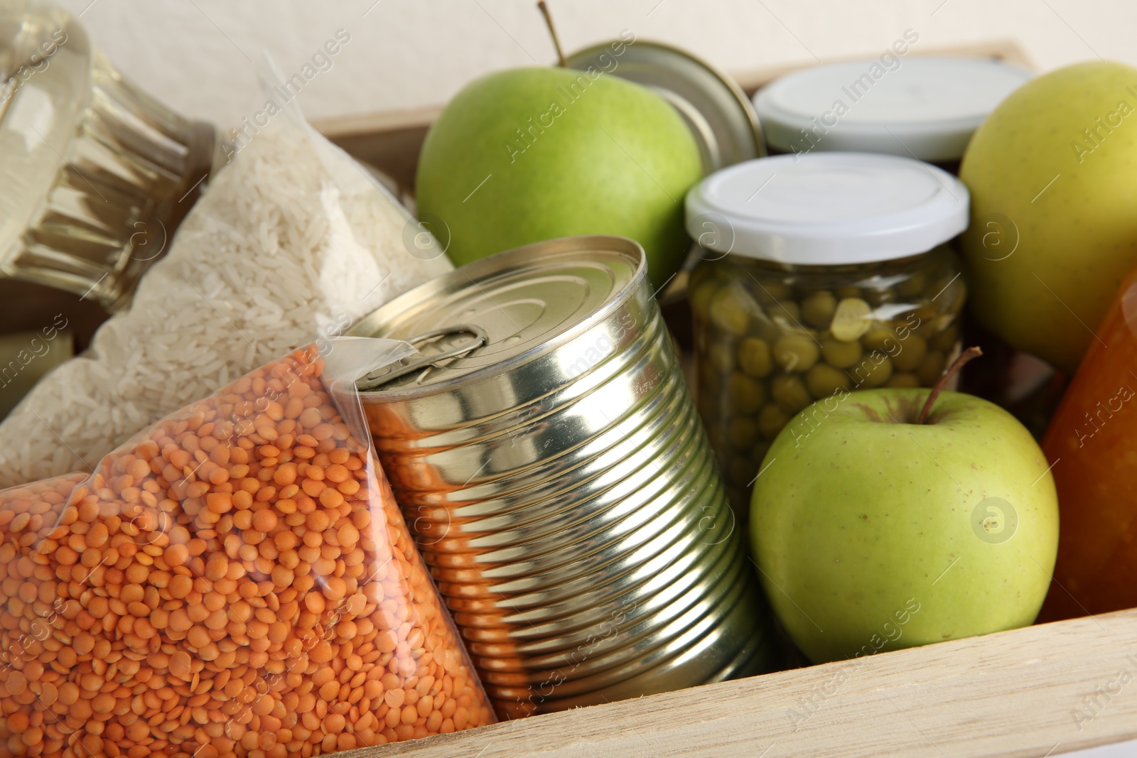 Photo of Different products in wooden crate on light background, closeup. Food donation