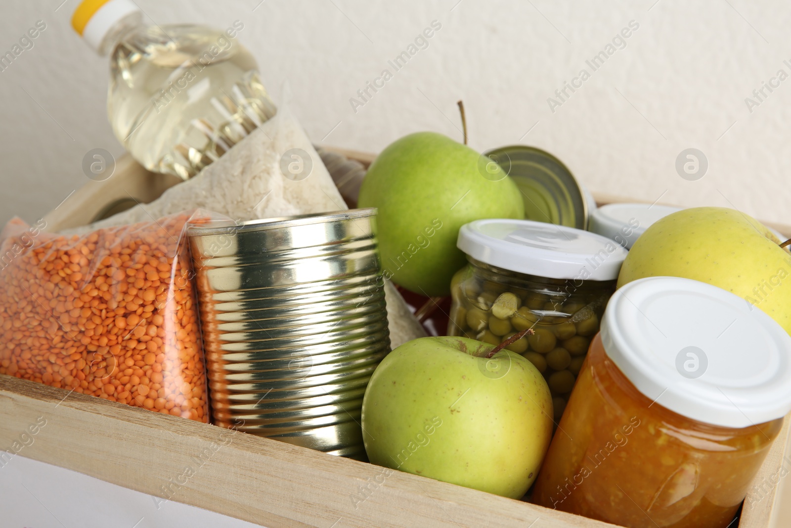 Photo of Different products in wooden crate on light background, closeup. Food donation