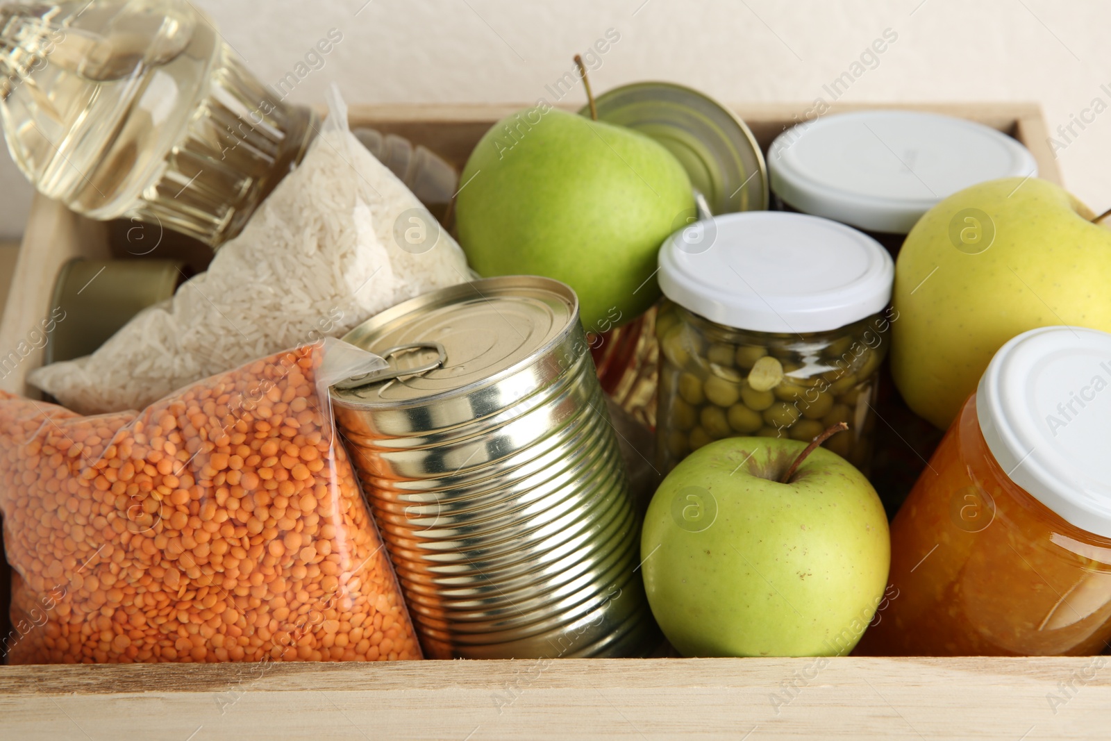 Photo of Different products in wooden crate on light background, closeup. Food donation