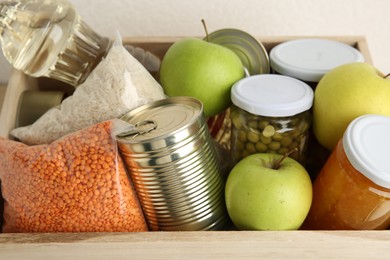 Photo of Different products in wooden crate on light background, closeup. Food donation