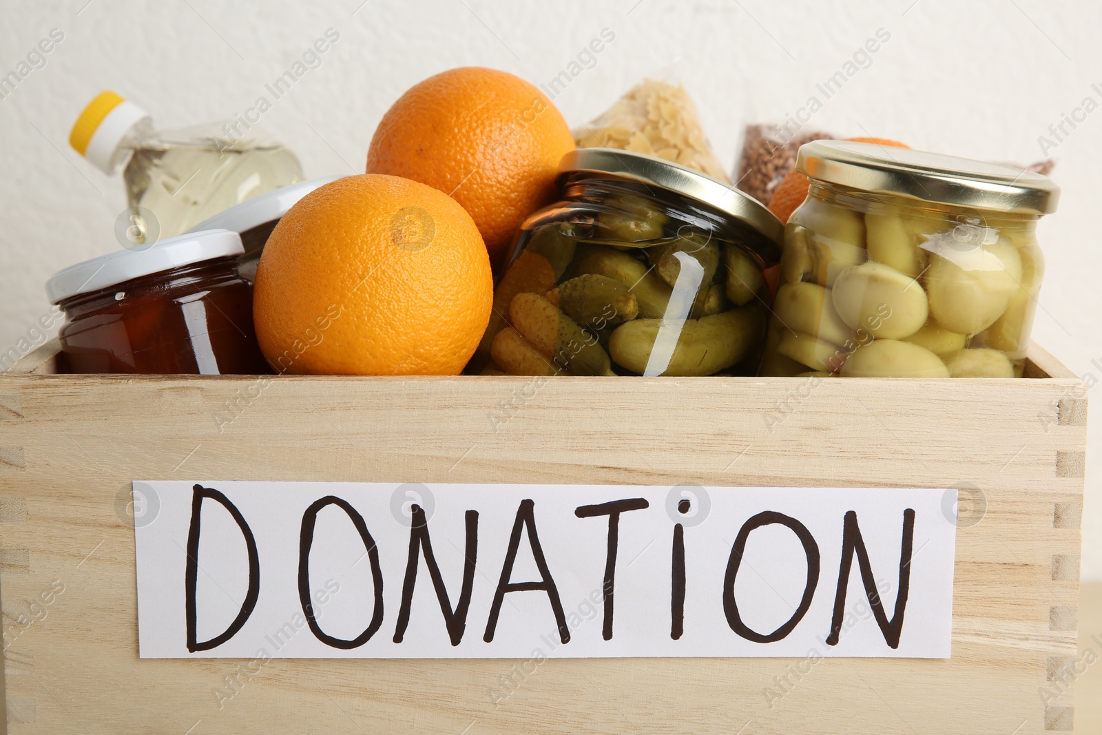 Photo of Donation food products in wooden crate on light background, closeup