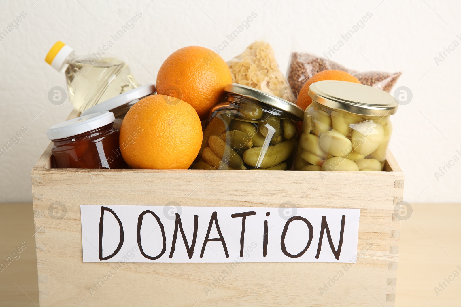 Photo of Different products in wooden crate on table, closeup. Food donation