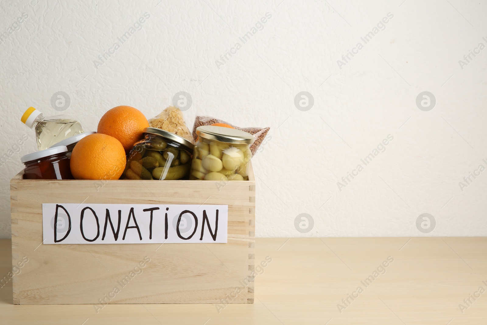 Photo of Different donation food products in crate on wooden table. Space for text