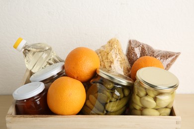 Photo of Different products in wooden crate on table, closeup. Food donation