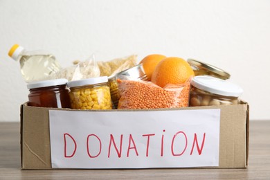 Photo of Different products in cardboard box on wooden table, closeup. Food donation