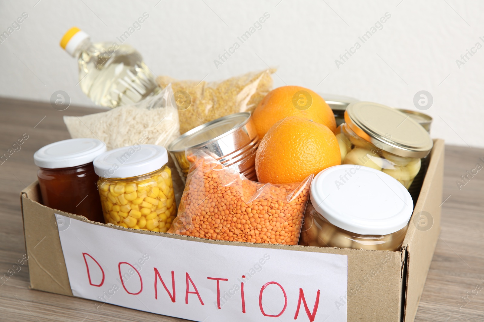 Photo of Different products in cardboard box on wooden table, closeup. Food donation