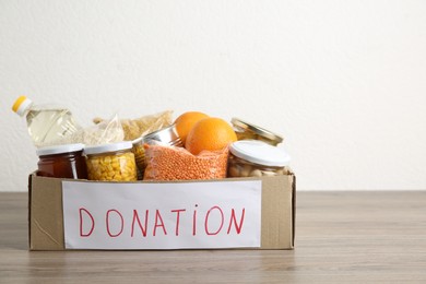 Photo of Different products in cardboard box on wooden table. Food donation